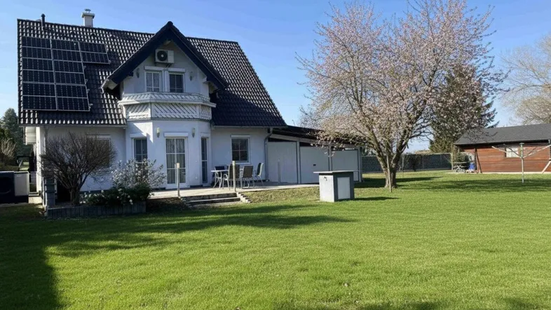 Großzügiger Gartenbereich mit Terrasse, blühendem Baum und Photovoltaikanlage auf dem Dach des Hauses.
