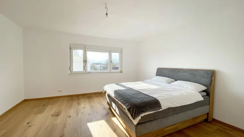 Helles Schlafzimmer mit natürlichem Holzboden und großem Fenster für viel Tageslicht.