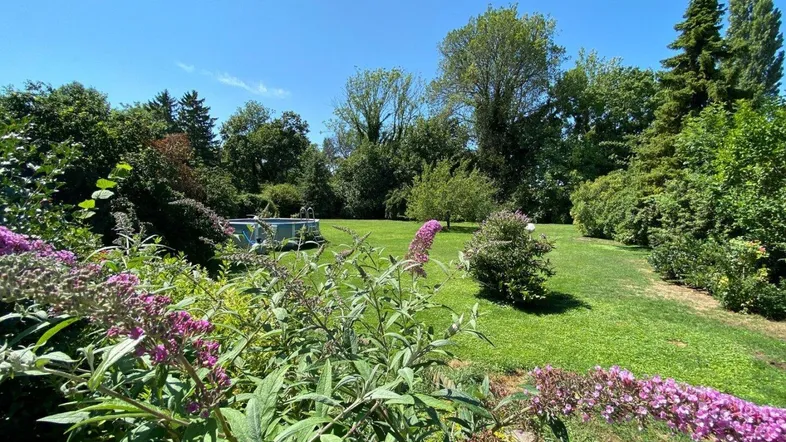 Weitläufiger Garten mit üppiger Vegetation, Rasenflächen und einem kleinen Pool im Hintergrund.