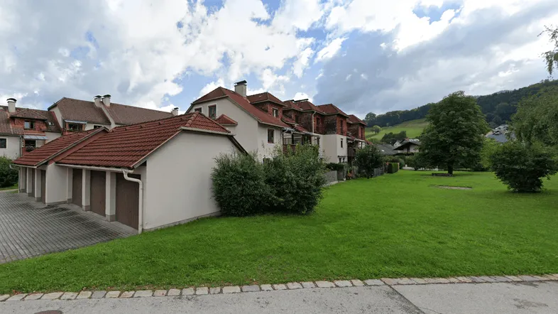 Reihenhäuser mit Garagen und gepflegter Grünfläche in ländlicher Umgebung mit Hügelblick.