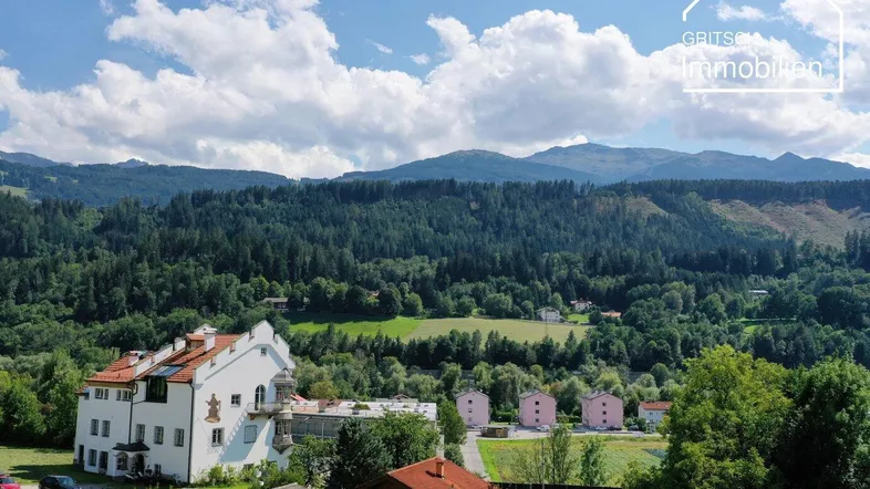 Panoramablick auf die umliegende Berglandschaft mit Wäldern und traditionellen Gebäuden unter blauem Himmel.