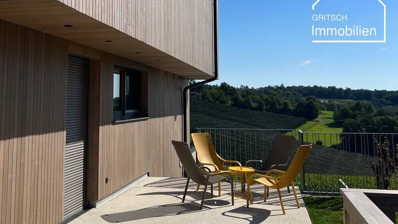 Moderne Holzfassade mit großer Terrasse, Gartenmöbeln und weitem Blick über die Weinberge.