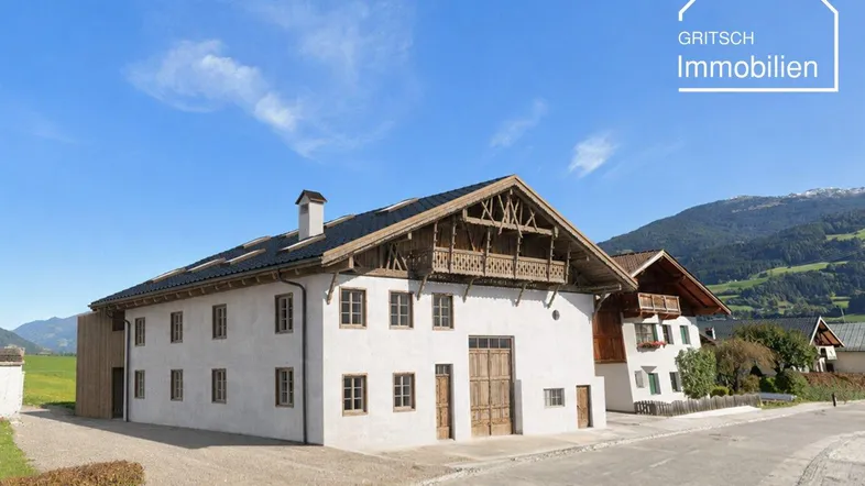 Großes traditionelles Gebäude mit Holzbalkonen und Ziegeldach, umgeben von einer bergigen Landschaft.