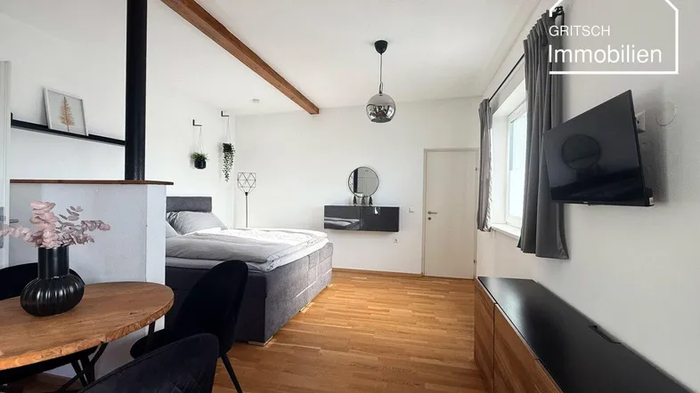Helles, offenes Wohn-Schlafzimmer mit Holzbalken, Parkettboden und Essbereich.