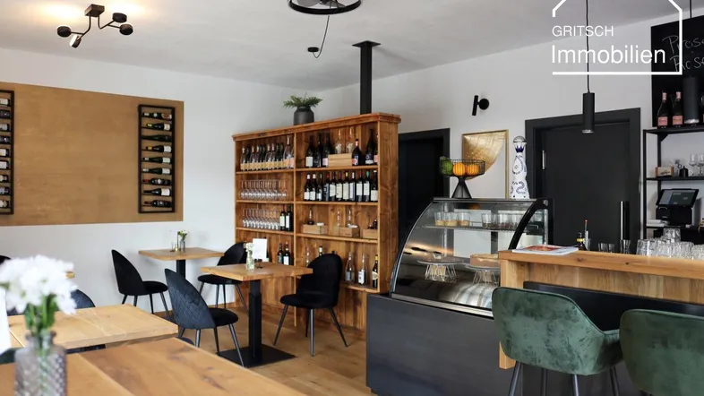 Heller Innenbereich eines Cafés oder einer Weinbar mit Holztischen, Weinregalen und einer Theke.