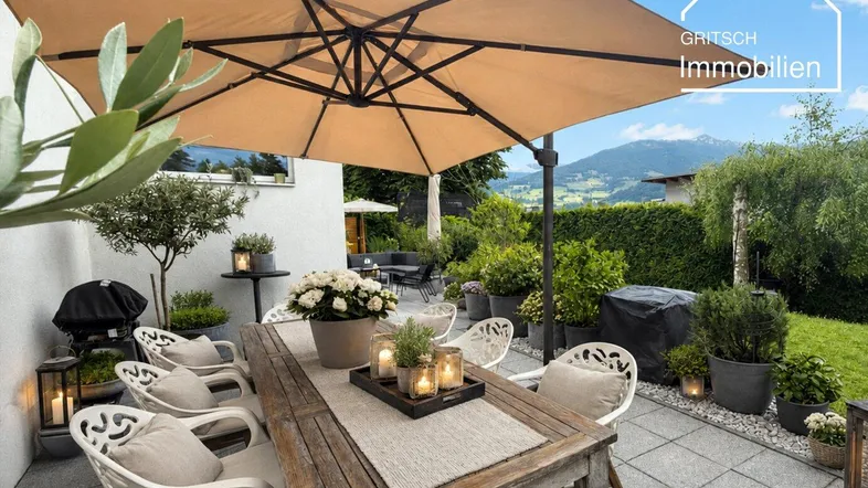 Gemütliche Terrasse mit großem Sonnenschirm, Esstisch und Blick auf die umliegende Berglandschaft.