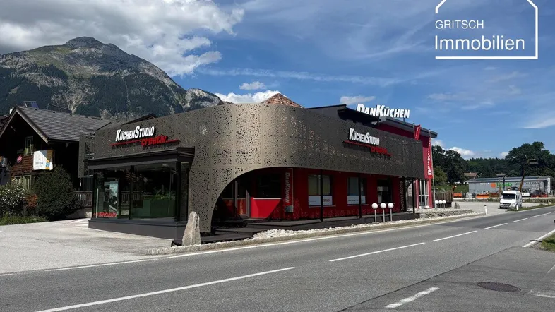 Modernes Geschäftsgebäude mit auffälliger Fassade und Bergkulisse unter blauem Himmel.