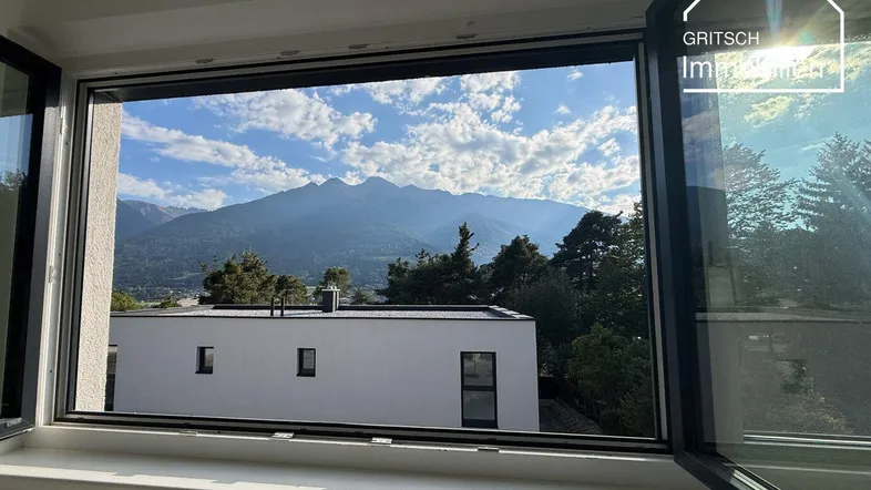 Blick aus einem Fenster auf eine beeindruckende Berglandschaft und ein modernes Gebäude.