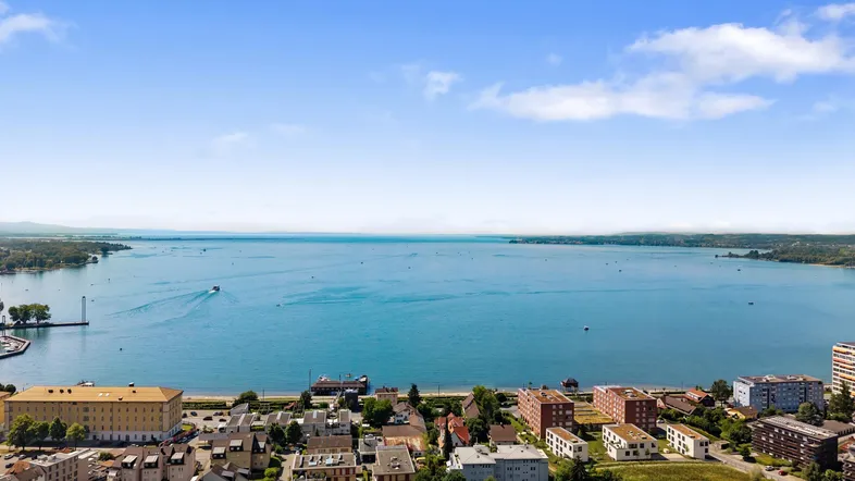 Panoramablick über den weiten See mit Uferbebauung und blauem Himmel.