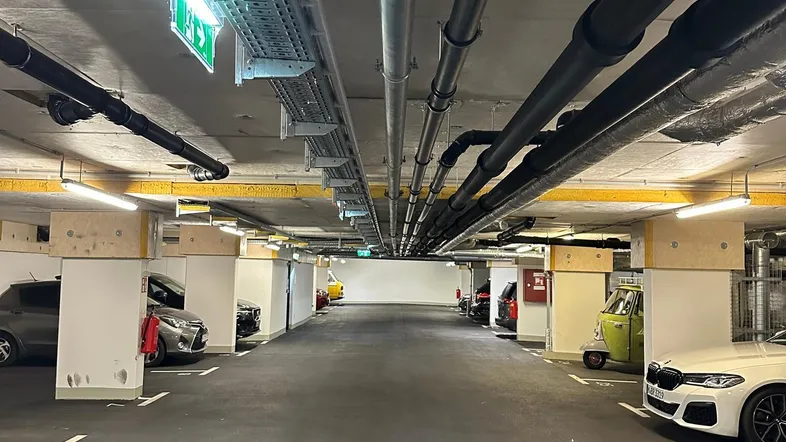 Geräumige Tiefgarage mit vielen Parkplätzen, sichtbaren Leitungen an der Decke und guter Beleuchtung.