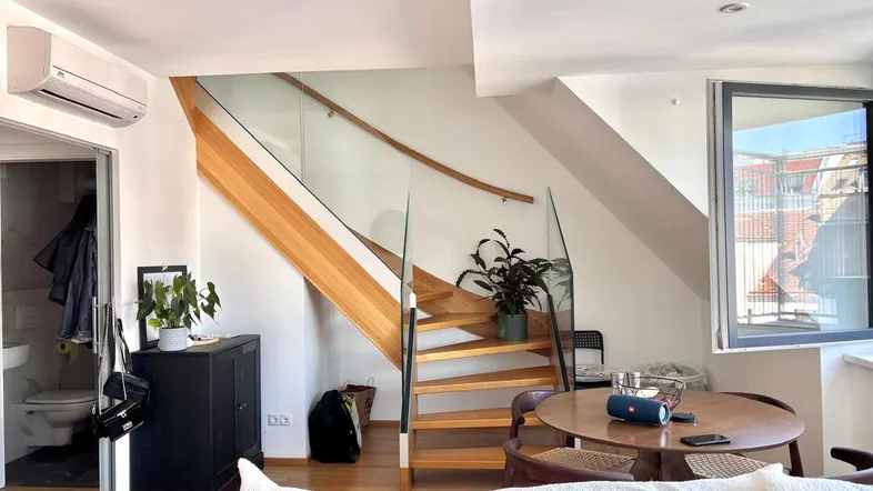 Heller Wohnbereich mit moderner Holztreppe, Glasgeländer und Klimaanlage, ideal für entspanntes Wohnen.
