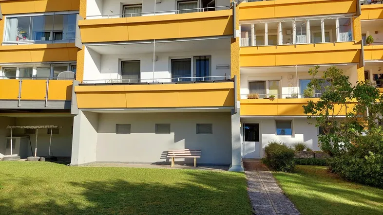 Mehrfamilienhaus mit gelben Balkonen und gepflegter Grünfläche im Vordergrund.