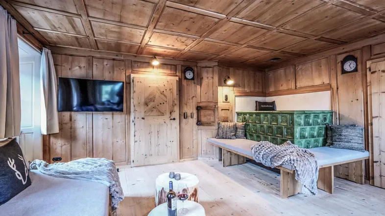Gemütliches Wohnzimmer im alpinen Stil mit Holztäfelung, Kachelofen und bequemen Sitzgelegenheiten.