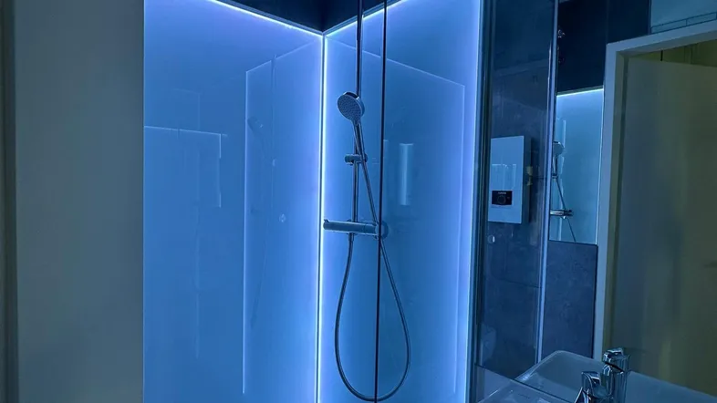 Modernes Badezimmer mit begehbarer Dusche, blauer LED-Beleuchtung und minimalistischem Waschbecken.