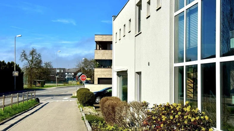Nahaufnahme der modernen Gebäudefassade mit großen Fenstern und einem Gehweg im Vordergrund unter blauem Himmel.