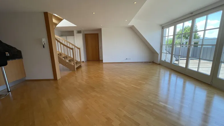 Geräumiges Wohnzimmer mit hellem Parkettboden, Dachschrägen und Zugang zu einer großen Terrasse.