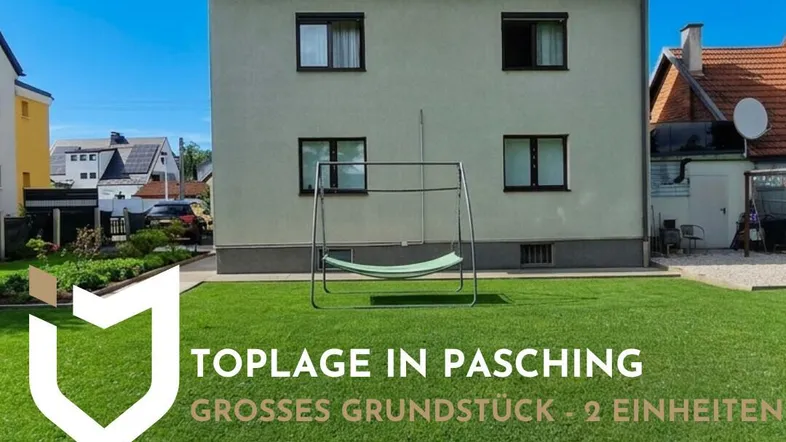 Hausfassade mit großem Rasenbereich und Schaukel im Vorgarten unter blauem Himmel.
