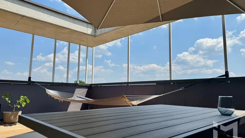 Geräumige Dachterrasse mit bequemer Hängematte, Esstisch und Sonnenschirm unter blauem Himmel.