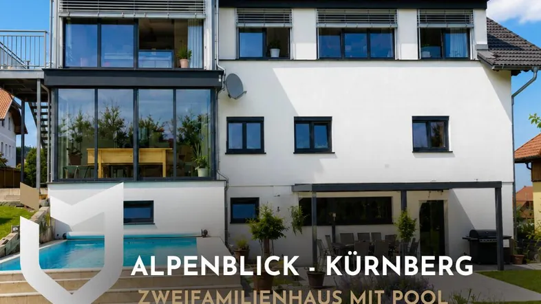 Modernes Zweifamilienhaus mit Pool und Garten, umgeben von grüner Landschaft unter blauem Himmel.