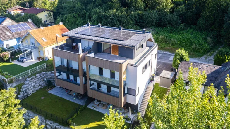 Moderne Wohnanlage mit Photovoltaikanlage auf dem Dach, umgeben von viel Grün und Bäumen.