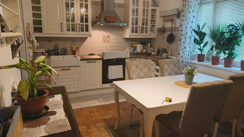 Gemütliche Küche mit hellem Essbereich, Holzparkett und Pflanzen am Fenster.