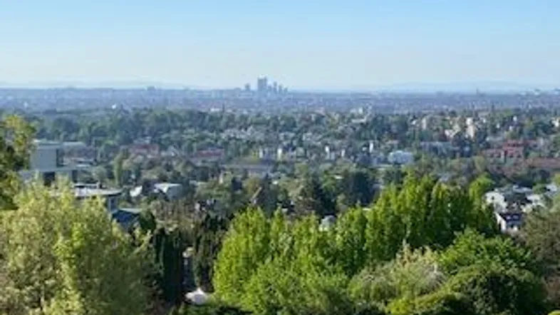 Weitläufiger Blick über eine grüne Landschaft mit einer Stadtkulisse am Horizont unter blauem Himmel.
