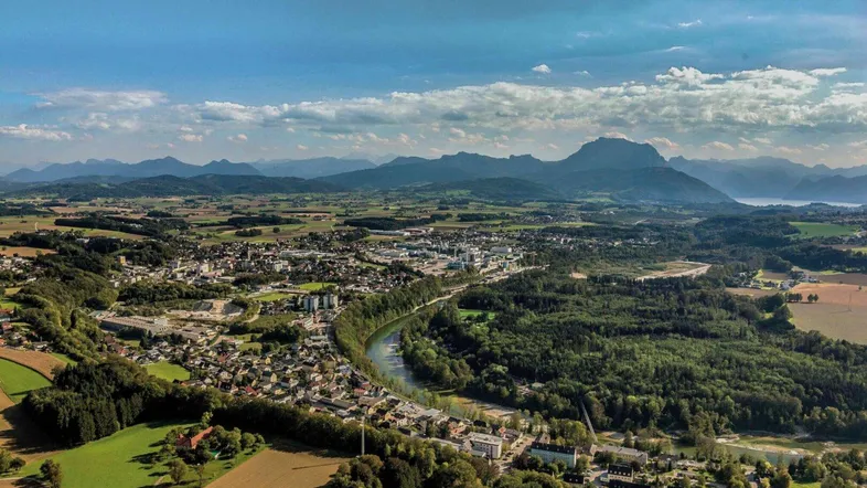 Luftaufnahme einer malerischen Stadt mit Fluss, umgeben von grünen Wäldern und Feldern, mit Bergen im Hintergrund.