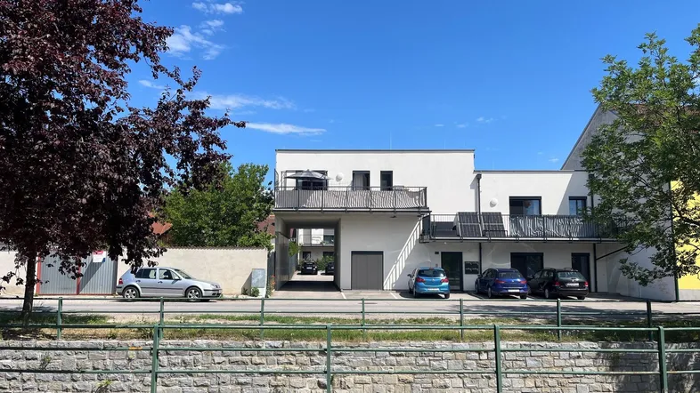 Modernes Mehrfamilienhaus mit Flachdach, Balkonen und Parkplätzen im Freien und unter dem Carport.