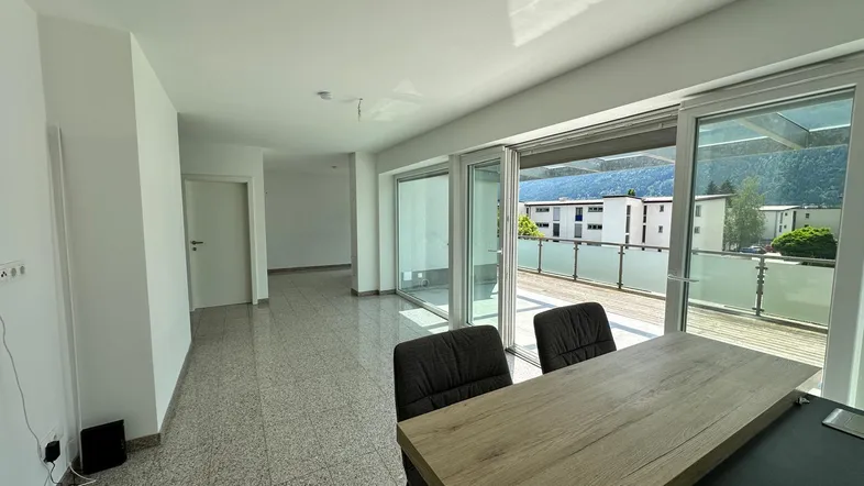 Heller Wohnbereich mit großen Schiebetüren, die auf eine Terrasse führen, und Blick auf die Berge.