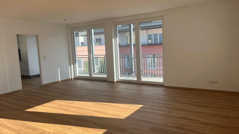 Helles Wohnzimmer mit Laminatboden und Zugang zu einem Balkon, durchflutet von natürlichem Sonnenlicht.