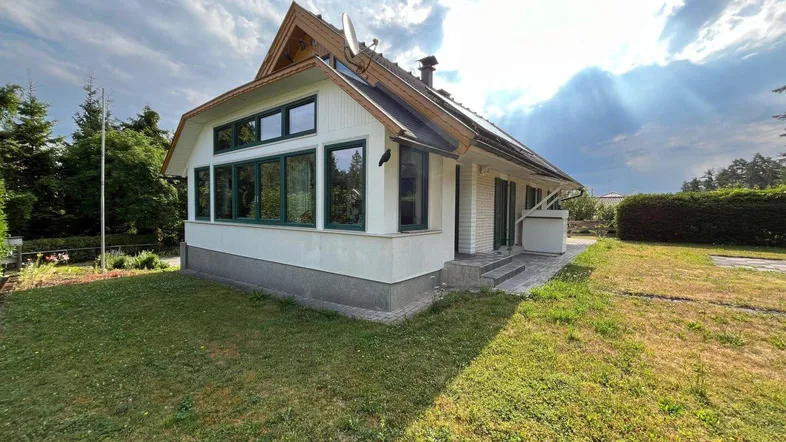 Charmantes Einfamilienhaus mit weißer Fassade, grünen Fensterrahmen und einem sonnigen Gartenbereich.