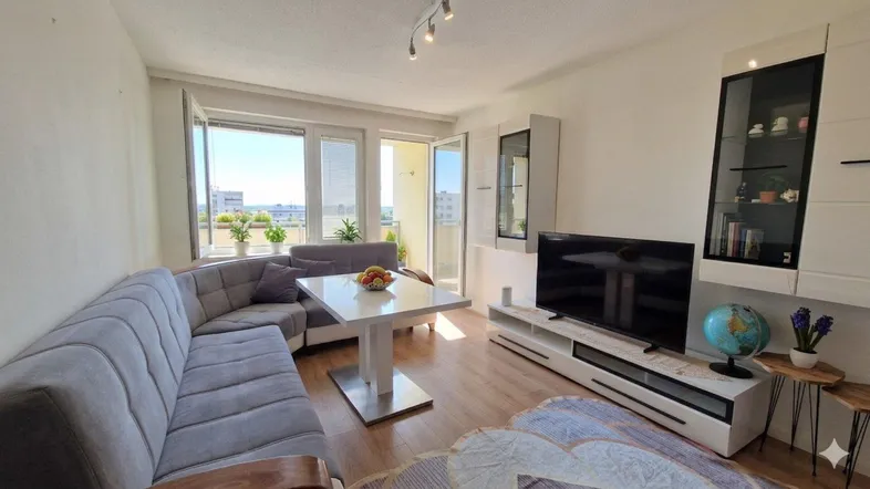 Helles Wohnzimmer mit bequemer Couch, Esstisch und Zugang zum sonnigen Balkon.