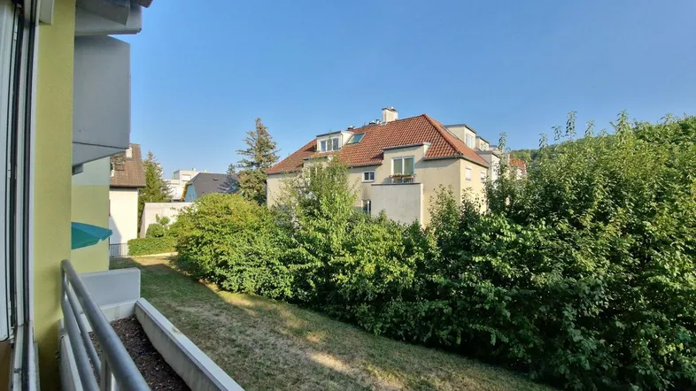 Blick vom Balkon auf die grüne Umgebung mit Hecken und einem gegenüberliegenden Gebäude.