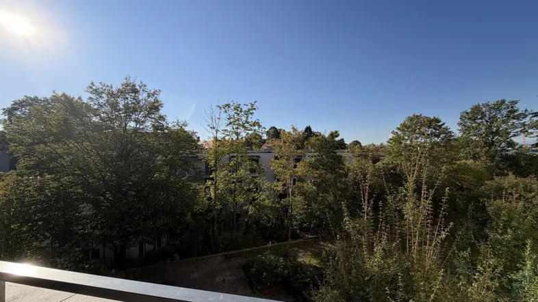 Sonniger Balkon mit weitem Blick über grüne Bäume und die umliegende Wohngegend.