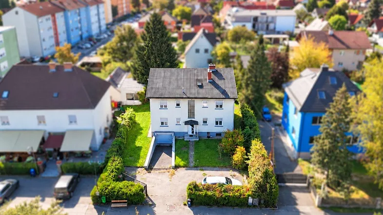 Luftaufnahme eines Einfamilienhauses mit Garten und umliegender Wohnbebauung in einer grünen Umgebung.