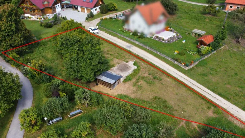 Luftaufnahme eines Grundstücks mit roter Markierung und umliegender Natur sowie angrenzenden Häusern.