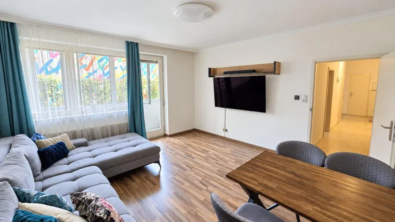 Helles Wohn- und Esszimmer mit modernem Sofa, Esstisch und Zugang zum Balkon.