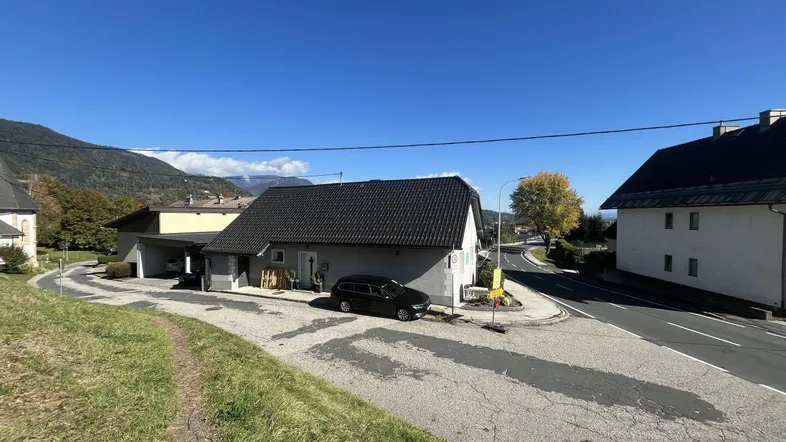 Einfamilienhaus mit dunklem Dach und Carport in ländlicher Umgebung mit Bergblick.
