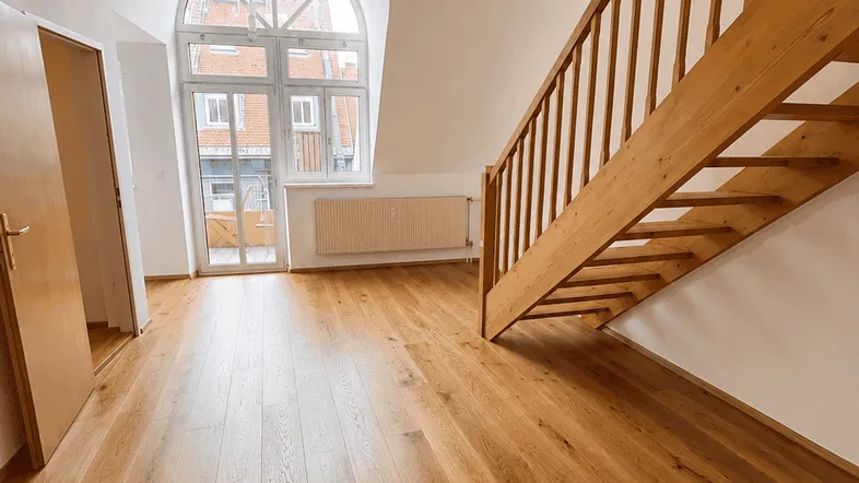 Heller offener Raum mit Holztreppe, großen Rundbogenfenstern und Parkettboden.