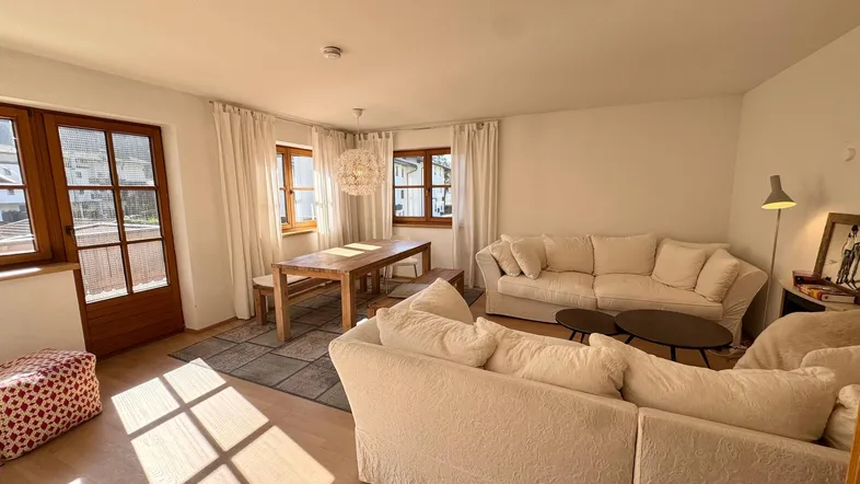 Helles Wohn- und Esszimmer mit bequemen Sofas, Holztisch und viel natürlichem Licht.