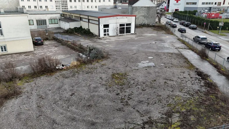 Luftaufnahme eines großen, unbefestigten Grundstücks mit Schotterfläche, umgeben von Gebäuden und einer Straße.