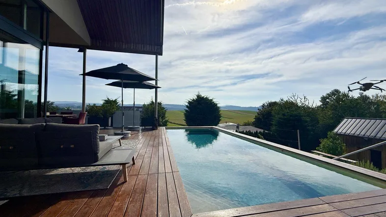 Geräumige Holzterrasse mit Infinity-Pool, bequemen Loungemöbeln und weitem Blick in die Landschaft.