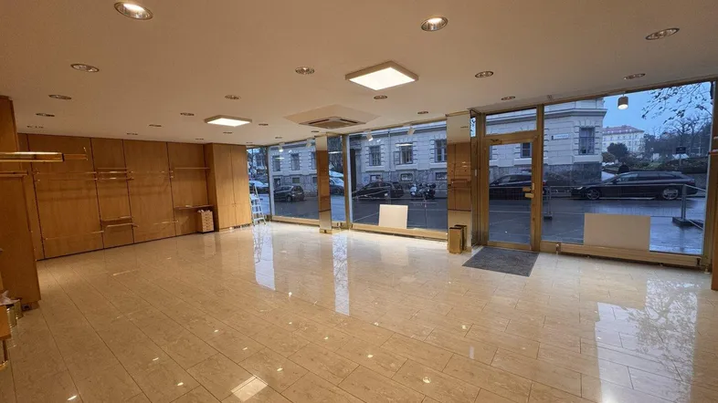 Geräumiger Gewerberaum mit großen Schaufenstern, hellen Fliesen und Holzvertäfelung, ideal für Einzelhandel oder Büro.