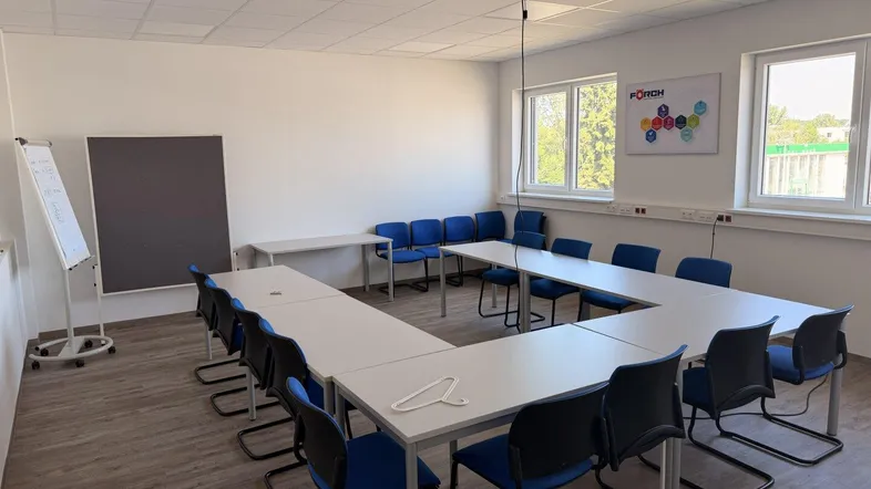 Geräumiger Konferenzraum mit U-förmiger Tischordnung, Projektor und großen Fenstern für natürliche Beleuchtung.