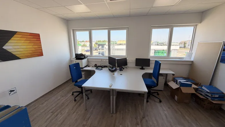 Modernes Büro mit zwei Arbeitsplätzen, Computern und Blick nach draußen durch große Fenster.