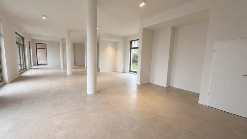 Geräumiger, heller Gewerberaum mit hohen Decken, vielen Fenstern und modernen Fliesenböden.