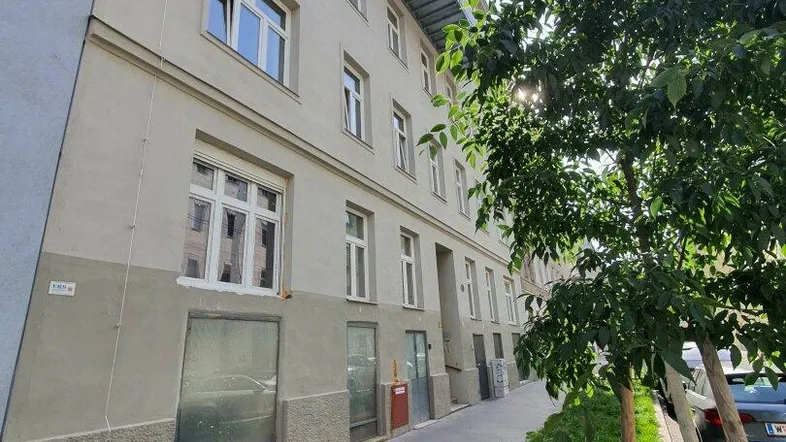 Fassade eines Mehrfamilienhauses mit mehreren Fenstern und einem Balkon an einem sonnigen Tag.