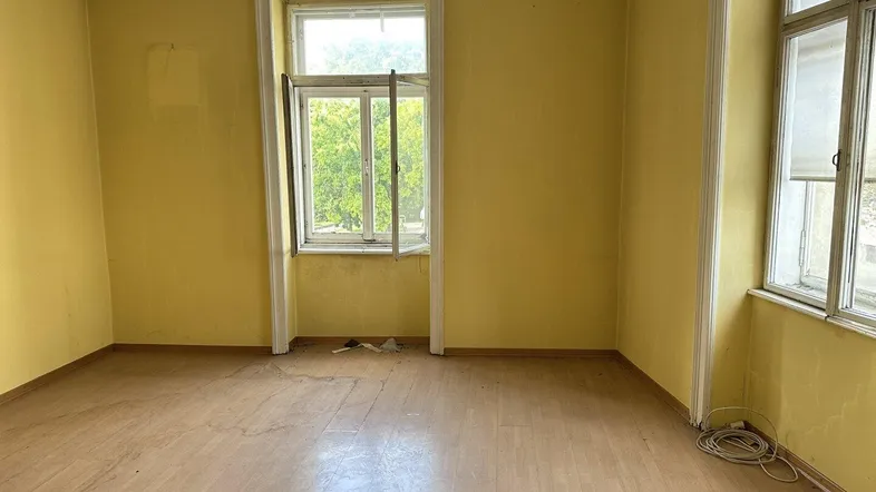Leeres Zimmer mit gelben Wänden und Laminatboden, bereit für Renovierung.