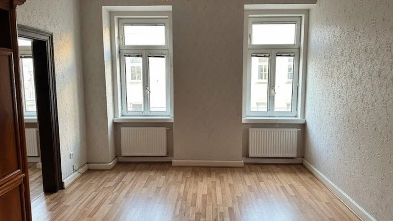 Helles Zimmer mit Laminatboden und zwei Fenstern, bereit zur individuellen Gestaltung.