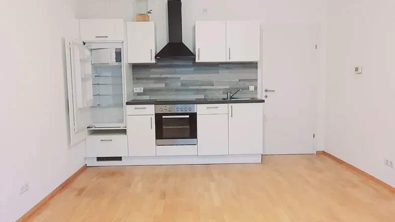Moderne Küchenzeile mit weißen Schränken, integriertem Kühlschrank und Holzboden in einem hellen Raum.